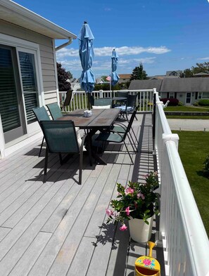 A covered outdoor deck with a table and chairs, a potted plant, and a small yellow container. - 🐋 Finback Beach House 🐋 Walk to Scarborough Beach, AC, Firepit, Bright & Open (Narragansett)