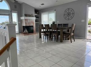 A dining area with a marble fireplace, dining table, chairs, and a view through a glass door. - 🐋 Finback Beach House 🐋 Walk to Scarborough Beach, AC, Firepit, Bright & Open (Narragansett)
