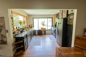 A kitchen with wooden cabinets, a refrigerator, and a window with a view of greenery.