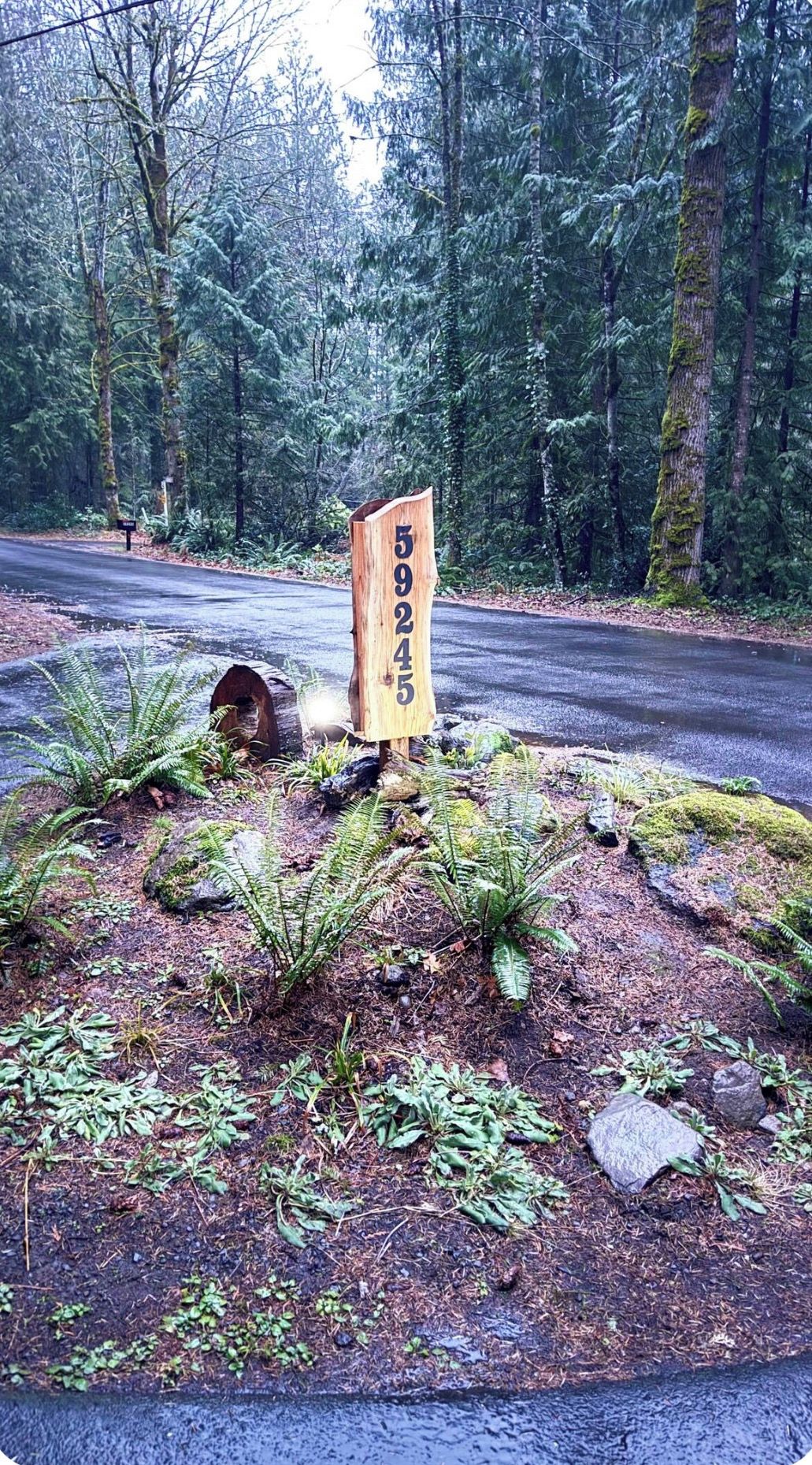 A wooden sign with numbers in a forested area beside a road.