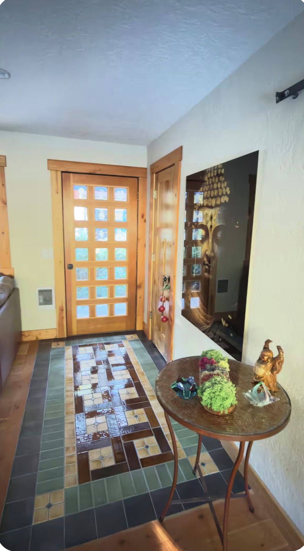 A hallway with a wooden door, a tiled floor, and a small round table with a plant and figurines.