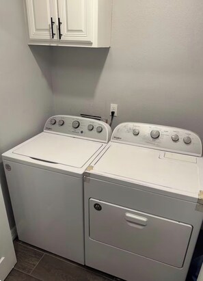 A laundry room with two stacked washer and dryer units, a white cabinet above, and a power outlet on the wall. - Spacious Beaumont Retreat Spacious + Home Gym (Beaumont)