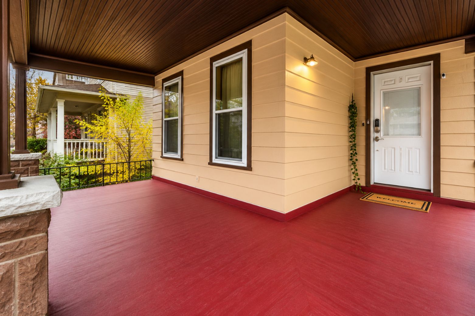 A covered porch with a red floor, a white door, and a small window.