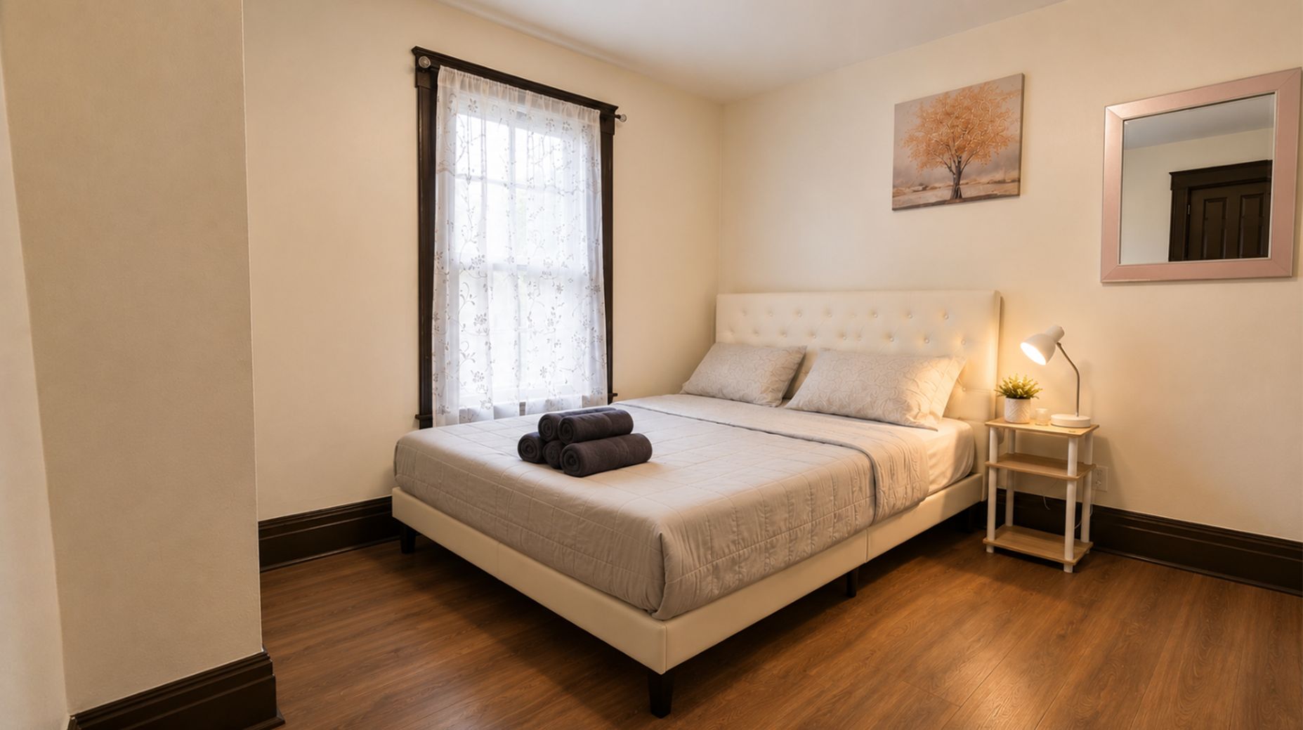 Une chambre à coucher bien rangée, avec un lit, une table de chevet dotée d’une lampe et une fenêtre avec des rideaux.