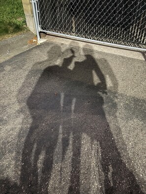 A shadow of a person on a paved surface, a metal fence, and a concrete wall. - Studio 6 (Eagan)