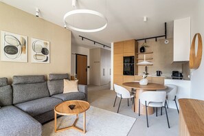 A modern living room with a grey sofa, a coffee table, and a dining area with a round table and chairs. - Towarowa Square V P&O Apartments (Warszawa)