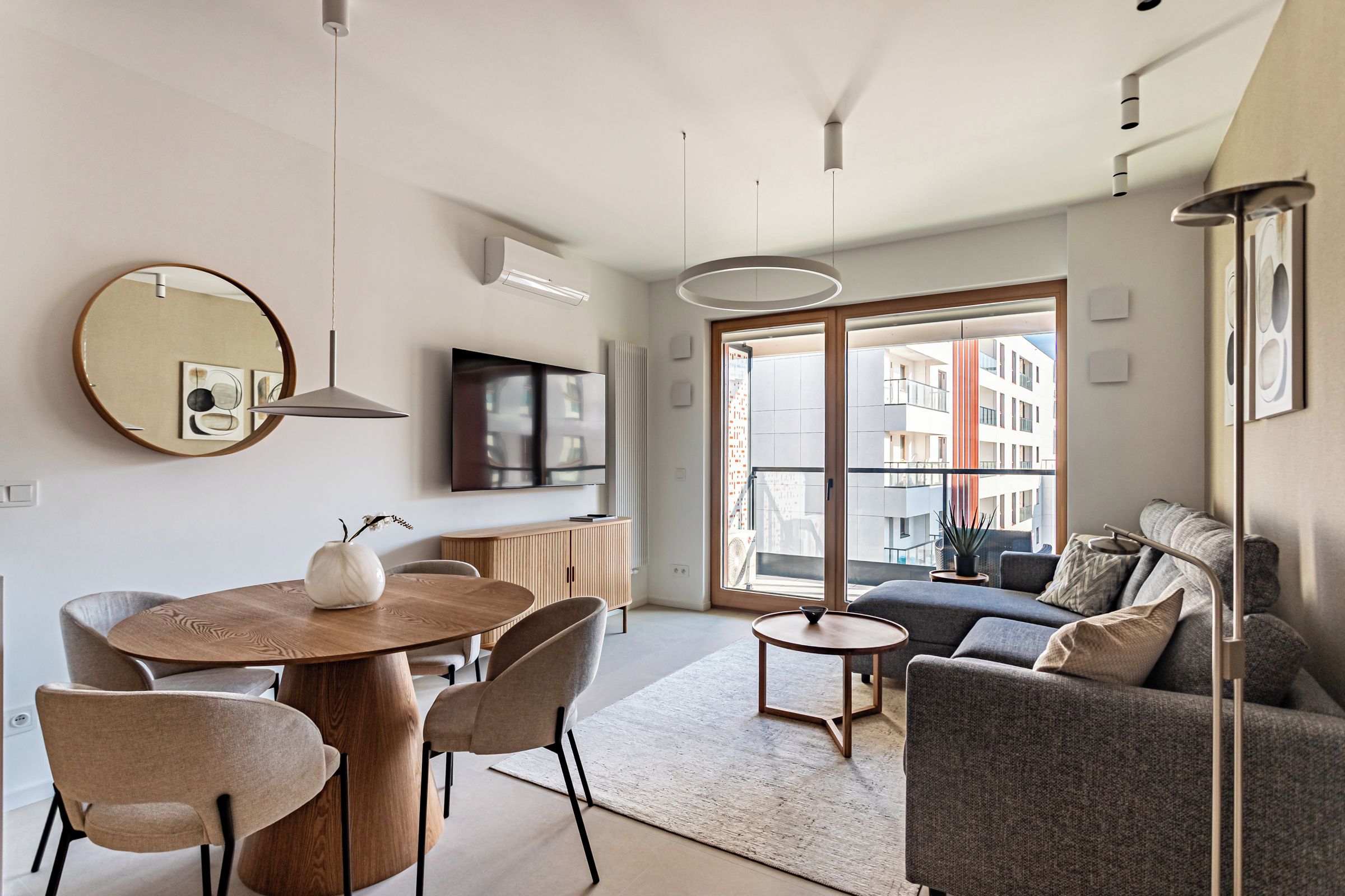 A modern living room with a dining area, a sofa set, a TV, and a large window offering a city view.