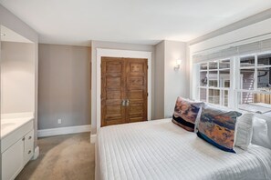 A bedroom with a large bed, a wooden wardrobe, a window with blinds, and a white dresser. - Fox Den on Historic French (Breckenridge)
