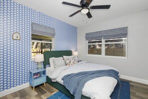 Ein Schlafzimmer mit einem Bett, einem Nachttisch, einem Deckenventilator und einem Fenster mit Jalousien.