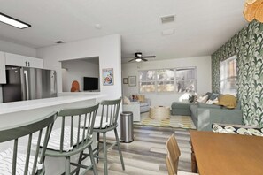 A modern kitchen with a stainless steel refrigerator, a dining area with green chairs, and a living room with a sofa and a patterned rug. - Saltwater Pool · 3BR 2BA · Near Clearwater Beach (Clearwater)