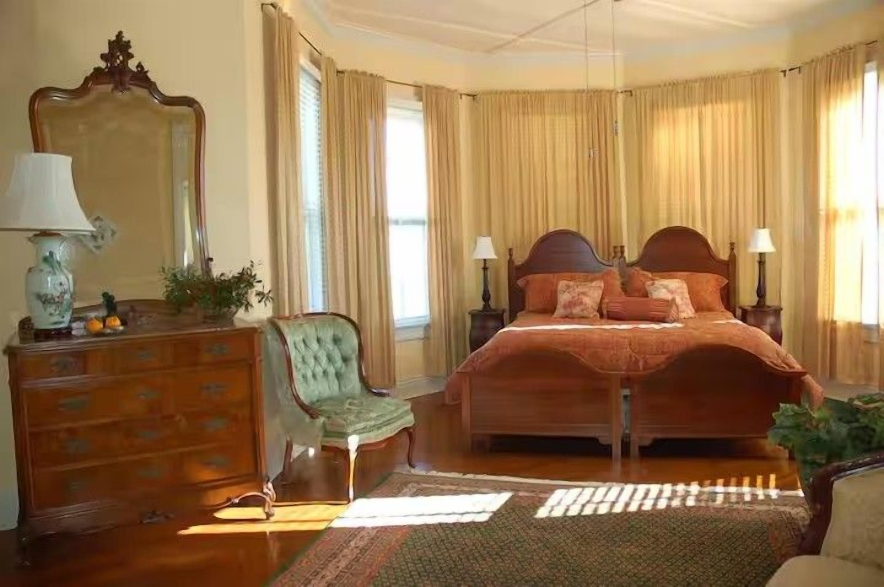 A bedroom with a double bed, a dresser, a chair, and a mirror.