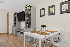 A modern living room with a white table, clear chairs, a flat-screen TV, and framed artwork on the wall. - Modern Downtown HR Condo | Walk to Waterfront (Hood River)