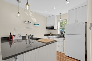 A modern kitchen with a central island, white cabinetry, a built-in oven, and a microwave. - Modern Downtown HR Condo | Walk to Waterfront (Hood River)