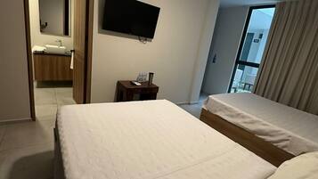 Habitación de hotel con dos camas, un televisor, ventilador de techo, baño visible a través de una puerta abierta y ventana con cortinas.