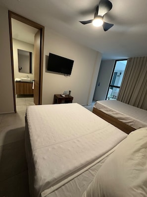 A hotel room with two beds, a television, a ceiling fan, a bathroom visible through an open door, and a window with curtains. - Hotel Concordia (Guadalajara)