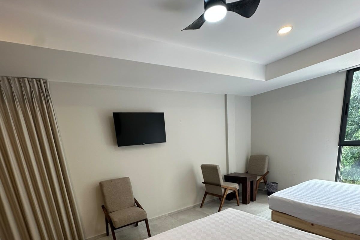 A hotel room with a bed, a desk, a chair, a television, and a ceiling fan.