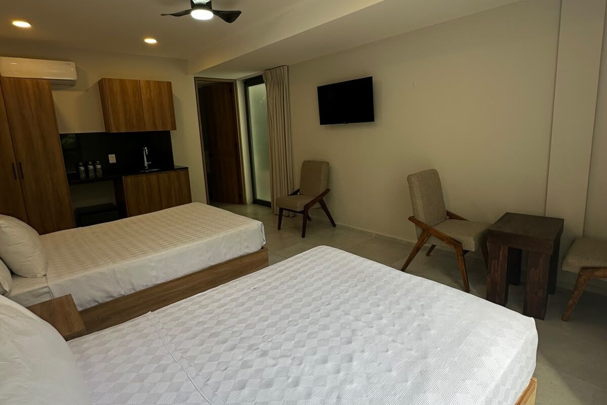 A hotel room with two beds, a TV, a ceiling fan, and a kitchenette.