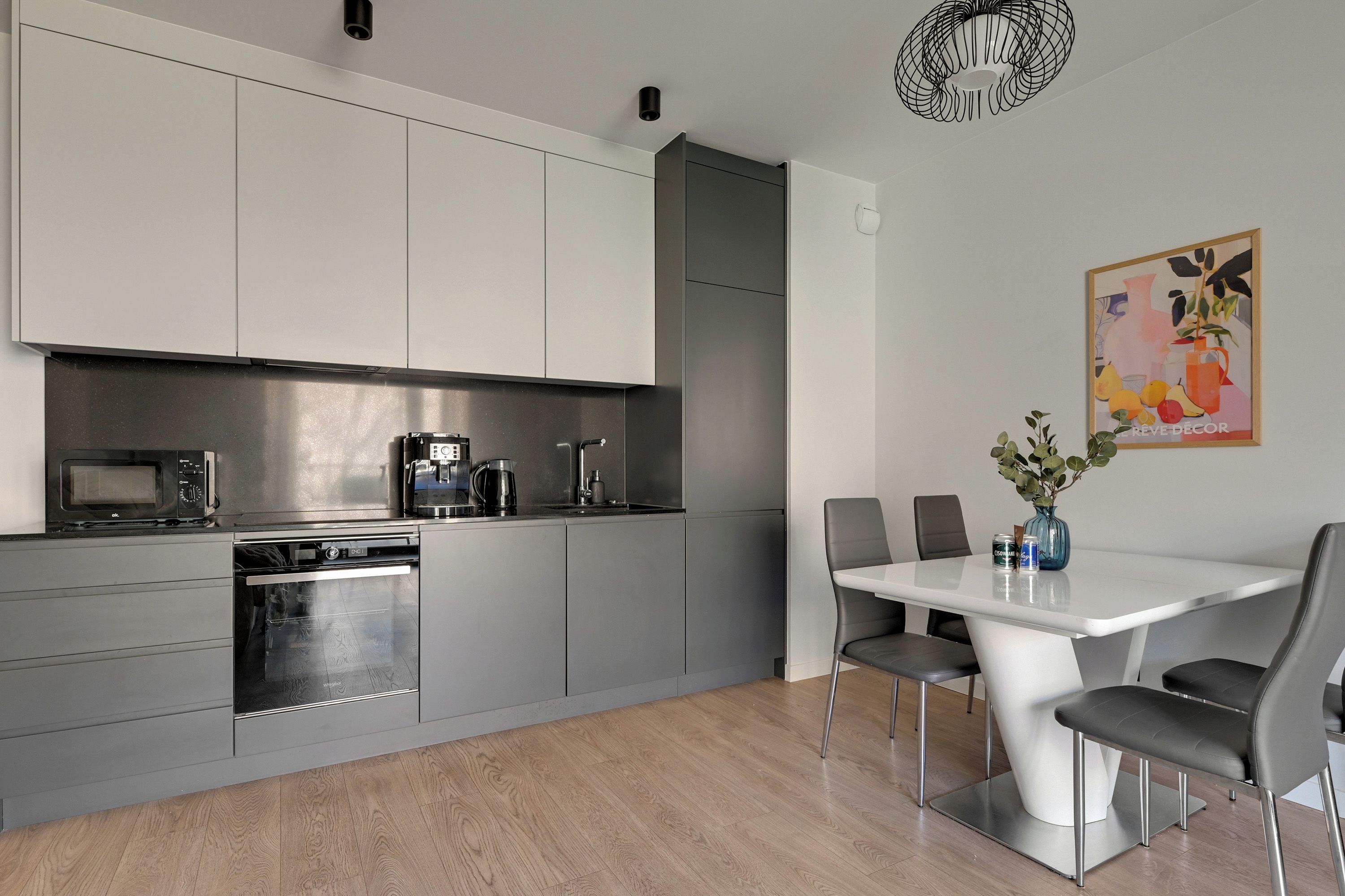 A modern kitchen with grey cabinets, a built-in oven, and a coffee machine.