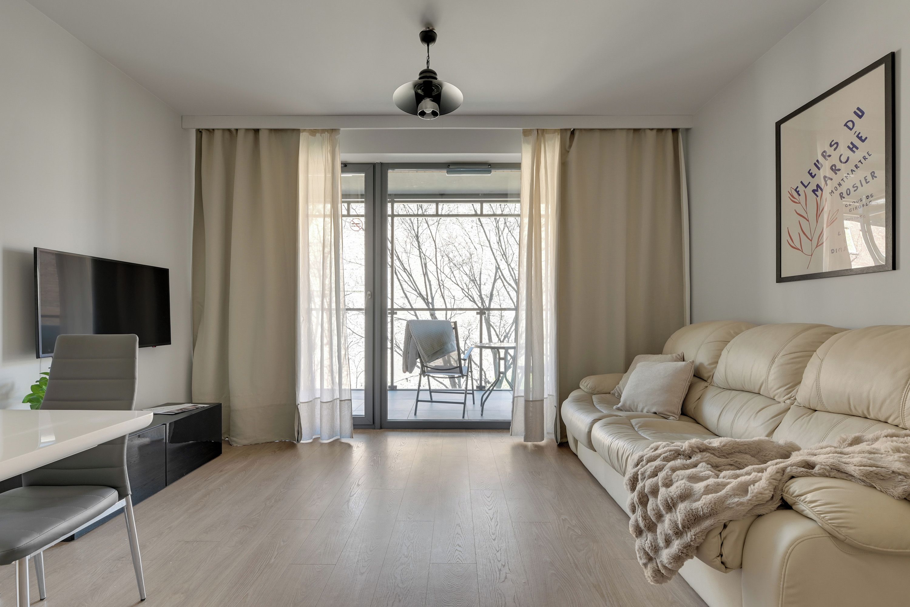 A modern living room with a sofa, a TV, a desk, and a balcony with a chair.