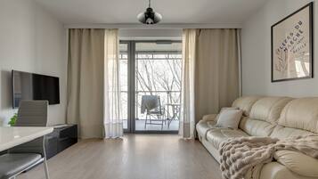 A modern living room with a sofa, a TV, a desk, and a balcony with a chair.