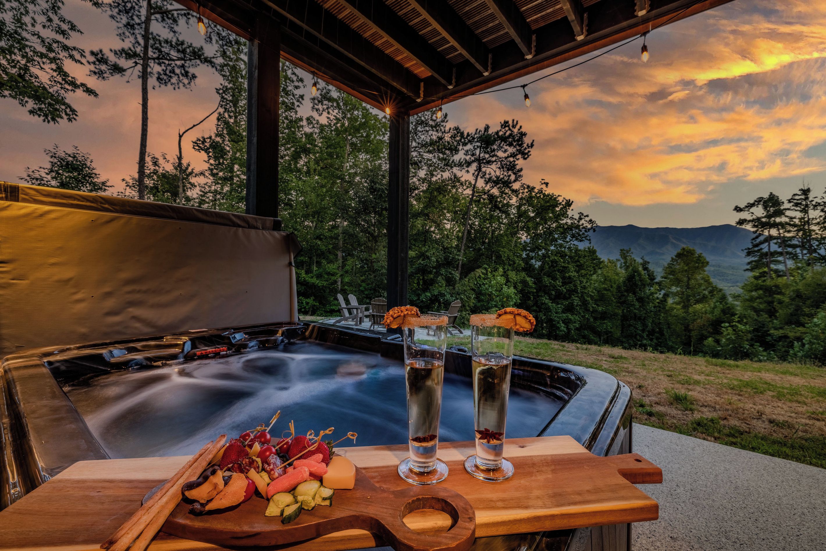 A hot tub with a wooden table in front, glasses of a beverage, and a fruit platter.