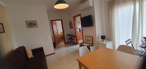 A compact living space with a dining area, a sofa, a TV mounted on the wall, and a window with curtains. - Refúgio na Falésia | beach | golf | Alfamar and Falésia (Albufeira)