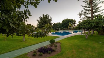 A landscaped garden with a swimming pool, a walking path, and various trees.