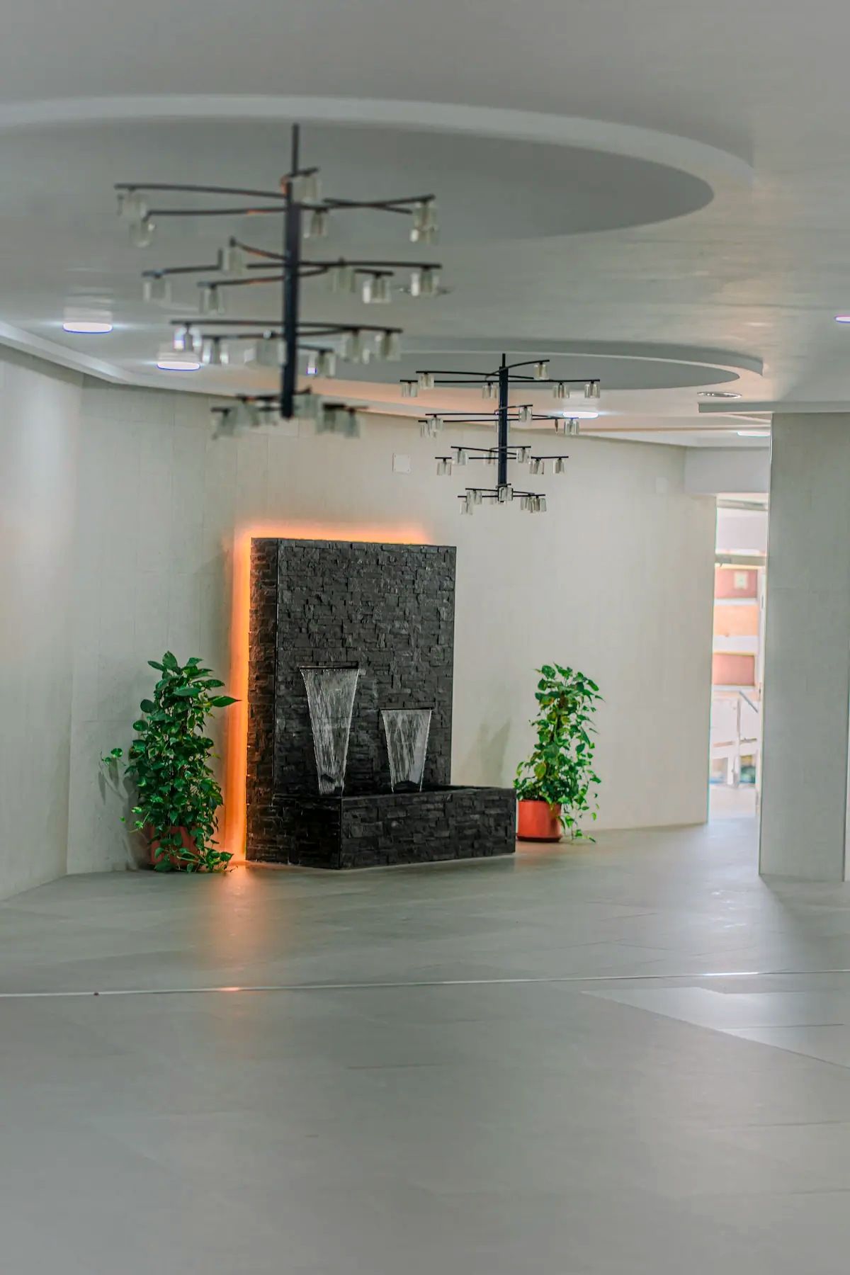 A modern lobby with a stone wall, two water features, and potted plants.