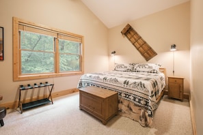 A bedroom with a large window, a bed with patterned bedding, a wooden bench, and a nightstand. - Bearway to Heaven 4BR, Slide, Hot Tub & Pool Table (Swanton)