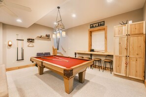 A pool table in a room with a ceiling fan, a bar area with stools, and wooden cabinets. - Bearway to Heaven 4BR, Slide, Hot Tub & Pool Table (Swanton)