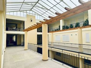 Ein geräumiger Innenhof mit hoher Decke und Tageslicht, mit einer zentralen Säule, einer Holzpergola und einem Balkon mit Topfpflanzen.