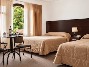 Habitación de hotel con dos camas, un escritorio con una silla, una lámpara y vistas a zonas verdes.
