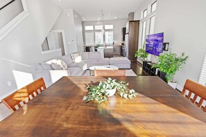Ein modernes Wohnzimmer mit einem großen Holzesstisch, einem grauen Ecksofa und einer Küche im Hintergrund.
