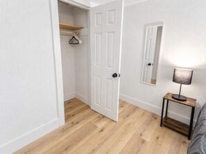 A room with a wooden floor, a white door, a small table with a lamp, and a mirror on the wall. - Historic Loft -3 I NRG    DT   MedCenter   FIFA (Houston)