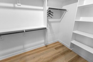 Ein Zimmer mit weißen Wänden, Holzboden und einem Metallgestell mit hängender Kleidung.