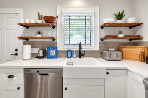 A modern kitchen with white cabinetry, a stainless steel dishwasher, a built-in oven, and a window with blinds. - Honky Tonk Heights Home I 2 Kings I EV I Fire Pit (Houston)