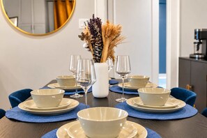 Ein Esstisch, gedeckt mit weißen Schüsseln, Tellern und Weingläsern, mit einer Vase getrockneter Blumen in der Mitte.