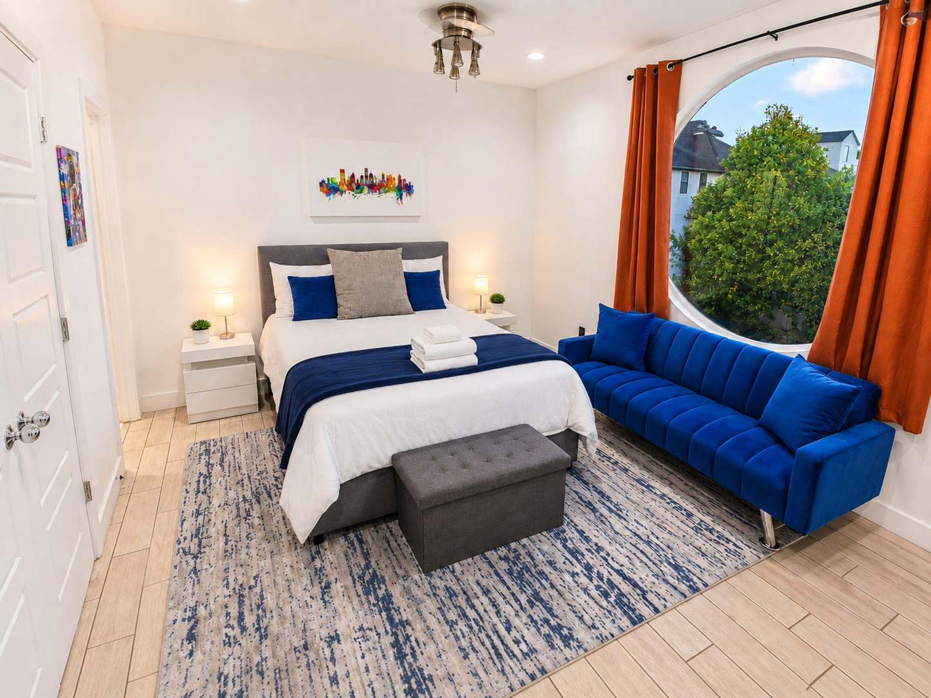 A modern bedroom with a bed, bedside tables, a blue sofa, and a window with curtains.