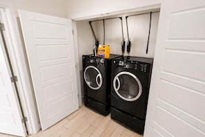 A laundry room with two black washing machines and a yellow detergent bottle on top. - Modern 4-Story Townhome  Med Center  Sleeps 8 (Houston)