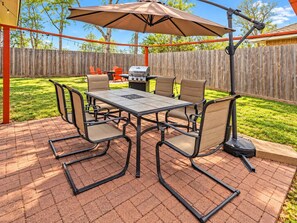 A patio with a table and chairs, a grill, and a wooden fence in the background. - 3BR Home with Firepit I Easy Access to NRG   FIFA (Houston)