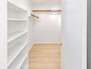 Ein begehbarer Kleiderschrank mit weißen Regalen, Holzboden und goldener Türgriff.