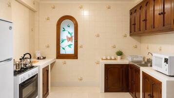 A kitchen with white tiles, wooden cabinets, a stove, a microwave, and a window with a floral design.
