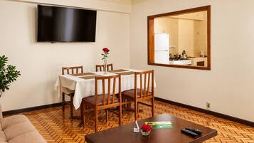 Une chambre d’hôtel équipée d’une table à manger, de chaises, d’un téléviseur, d’un miroir et d’un canapé.