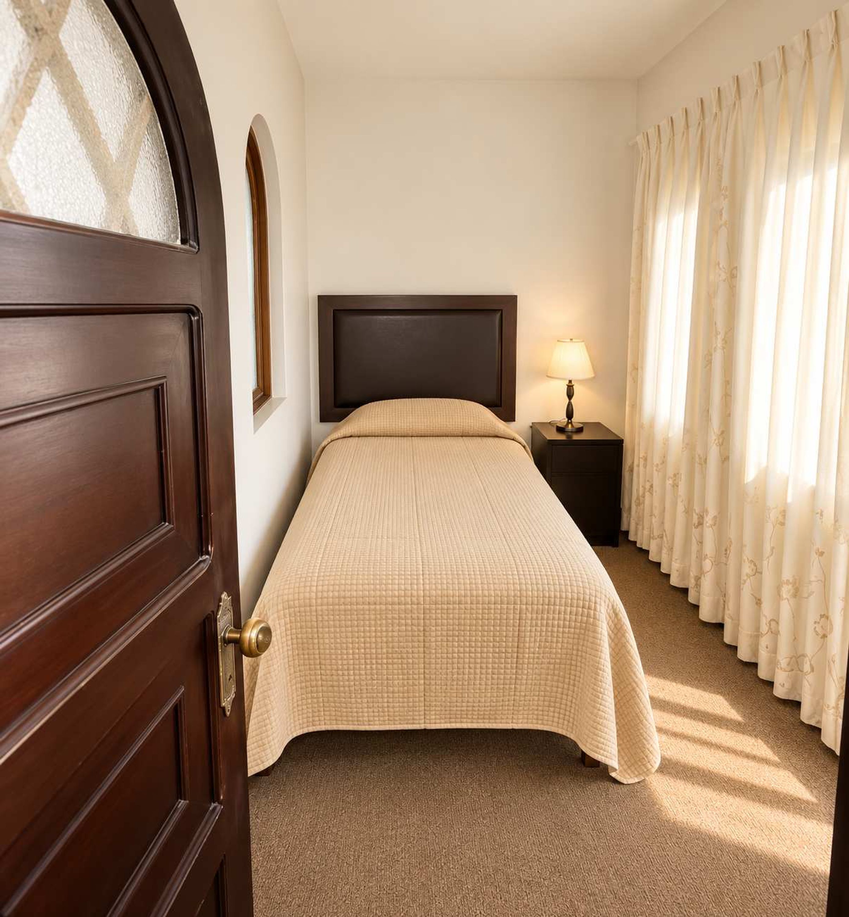 A hotel room with a bed, a nightstand with a lamp, a door, and curtains.