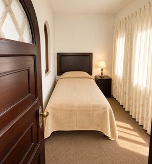 Een hotelkamer met een bed, nachtkastje met lamp, een deur en gordijnen.
