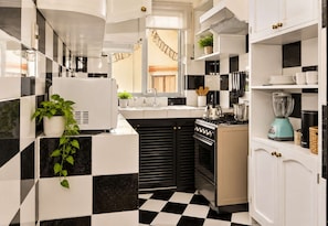 Una cocina compacta con piso a cuadros blanco y negro, estufa, lavaplatos y refrigerador.