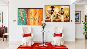 A modern living room with two white armchairs, a red rug, and two large paintings on the wall.