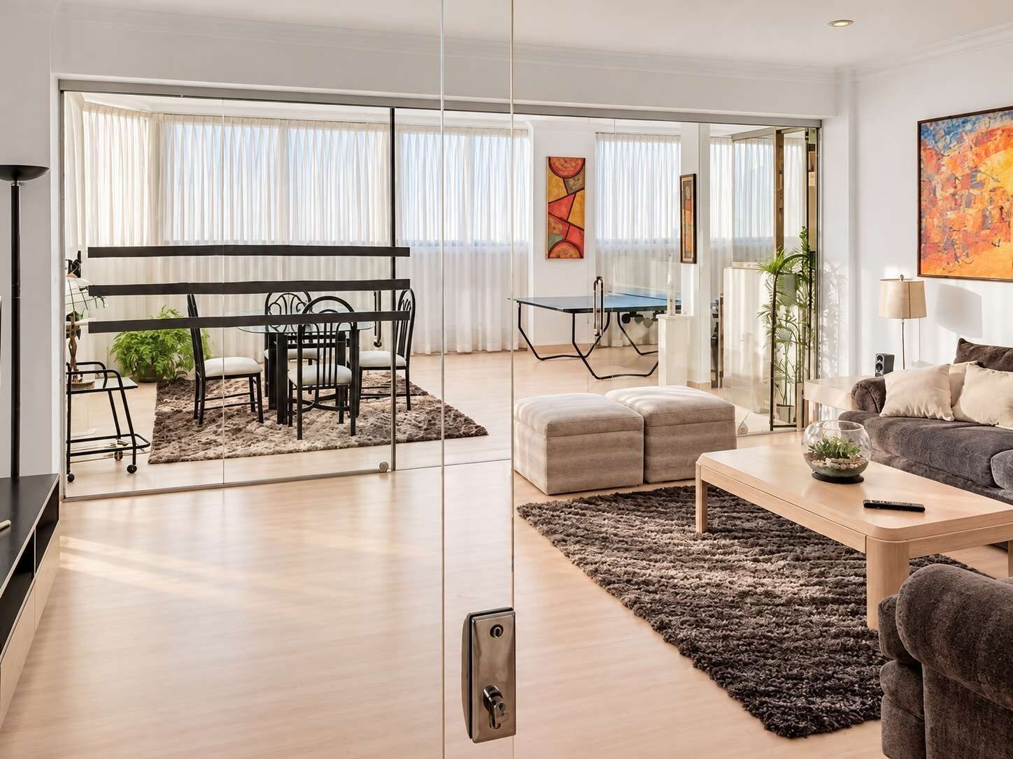 A modern living room with a sofa, ottoman, coffee table, and a dining area with a table and chairs.