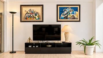 A modern living room with a flat-screen TV, a black entertainment unit, a floor lamp, and two framed artworks on the wall.