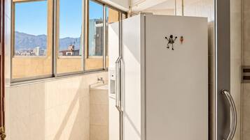 Eine moderne Küche mit einem Einbaukühlschrank, einem Fenster mit Blick auf Gebäude und einem Fliesenboden.